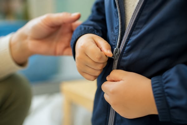 ABA therapist using prompt fading to help an autistic child zip a jacket.